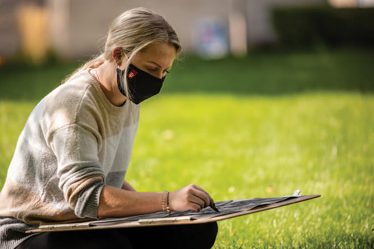 IU South Bend art student working on drawing outside seated in grass