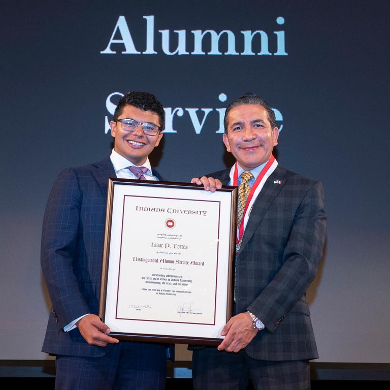 Isaac Torres holds up Distinguished Alumni Service Award with family member